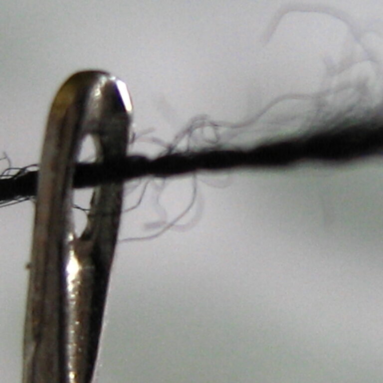 close-up picture of a frayed, dark thread going through the eye of a needle.